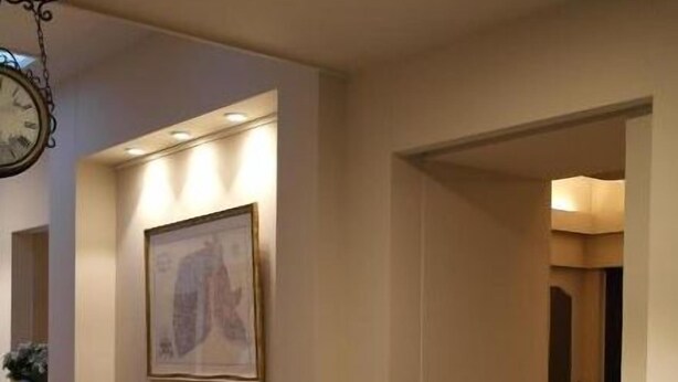 Un pasillo con un cuadro enmarcado en la pared, un reloj y una puerta que da a otra habitación.