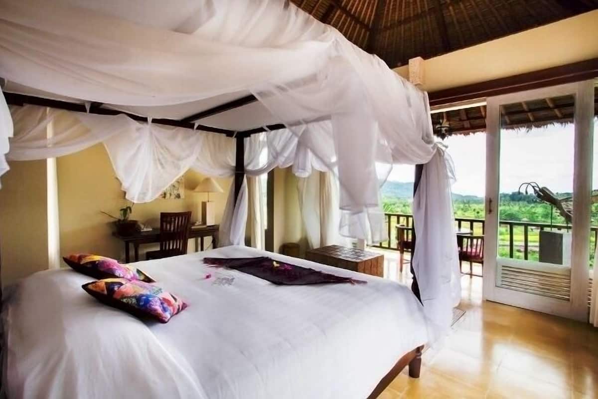 A bedroom with a canopy bed, a view of the outdoors, and a balcony with chairs.