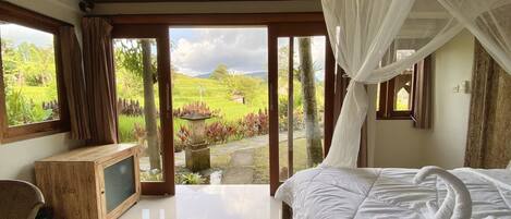 A bedroom with a bed, a television, and a view of a lush garden.