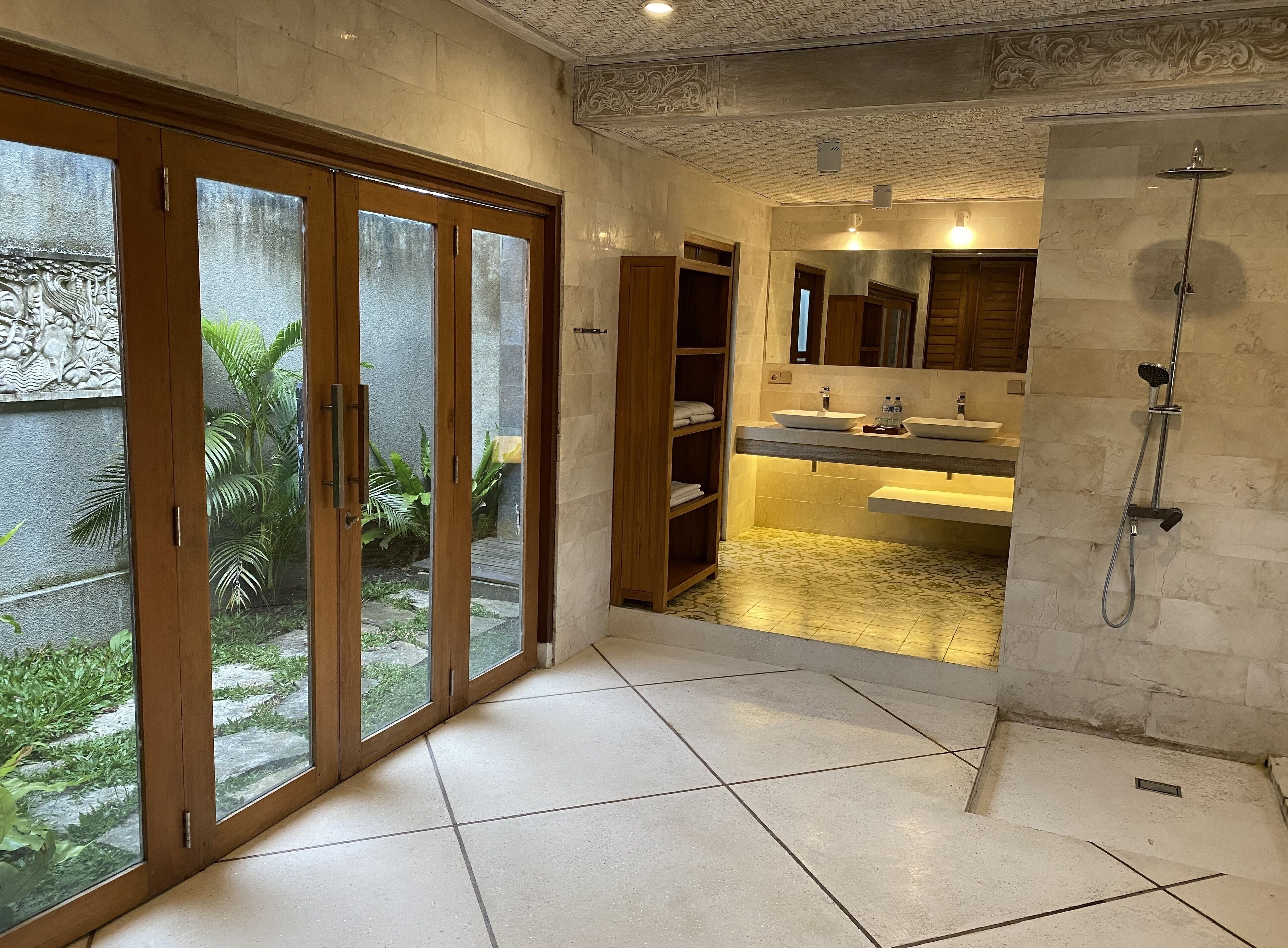 A bathroom with a large sliding glass door leading to a garden, a built-in sink, and a shower.