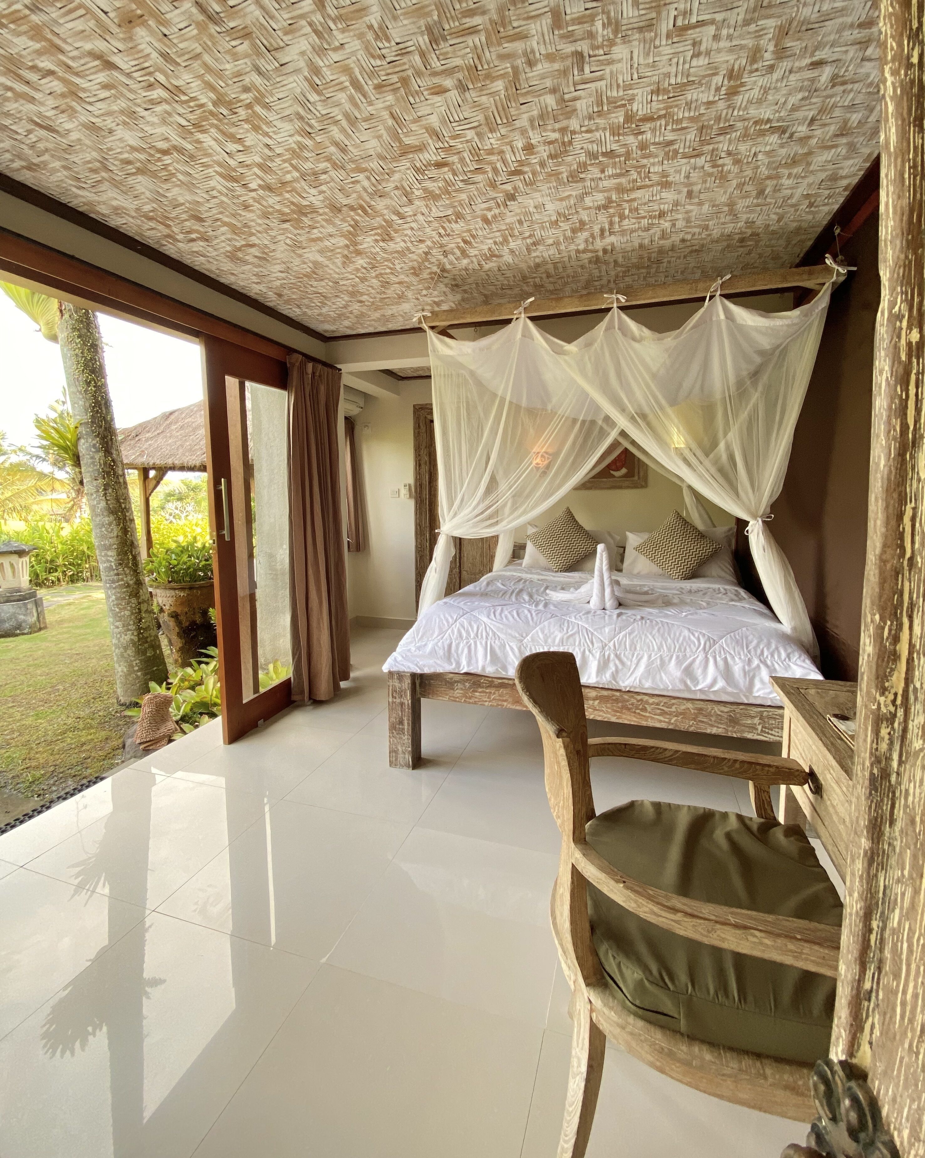 Un dormitorio con cama bajo dosel, una silla de madera y vistas al jardín.