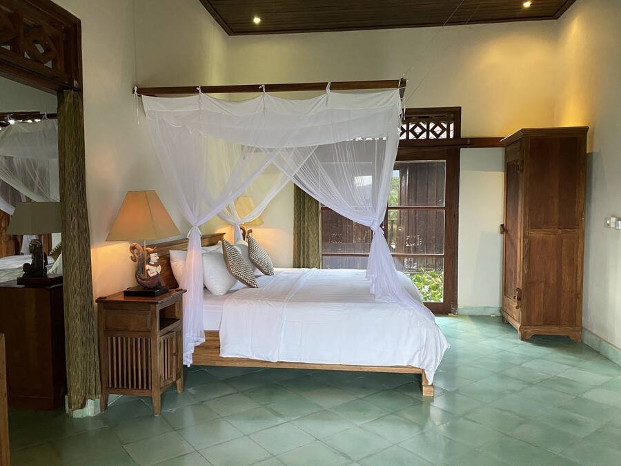 A bedroom with a four-poster bed, a nightstand, a lamp, and a wooden wardrobe.