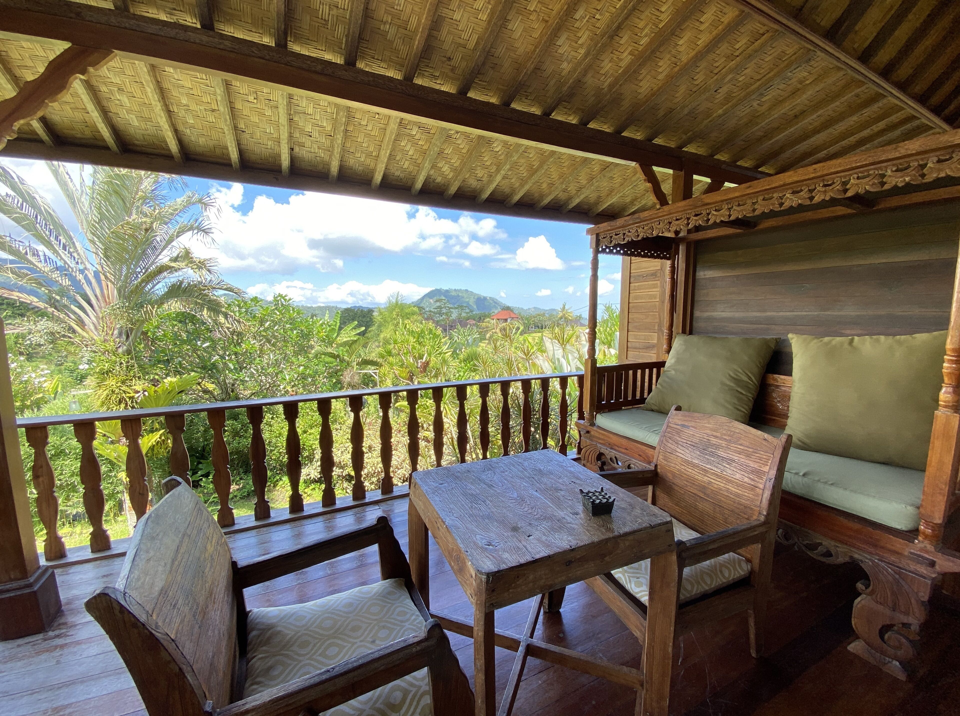 A wooden balcony with a woven ceiling, a cushioned bench, and a table.