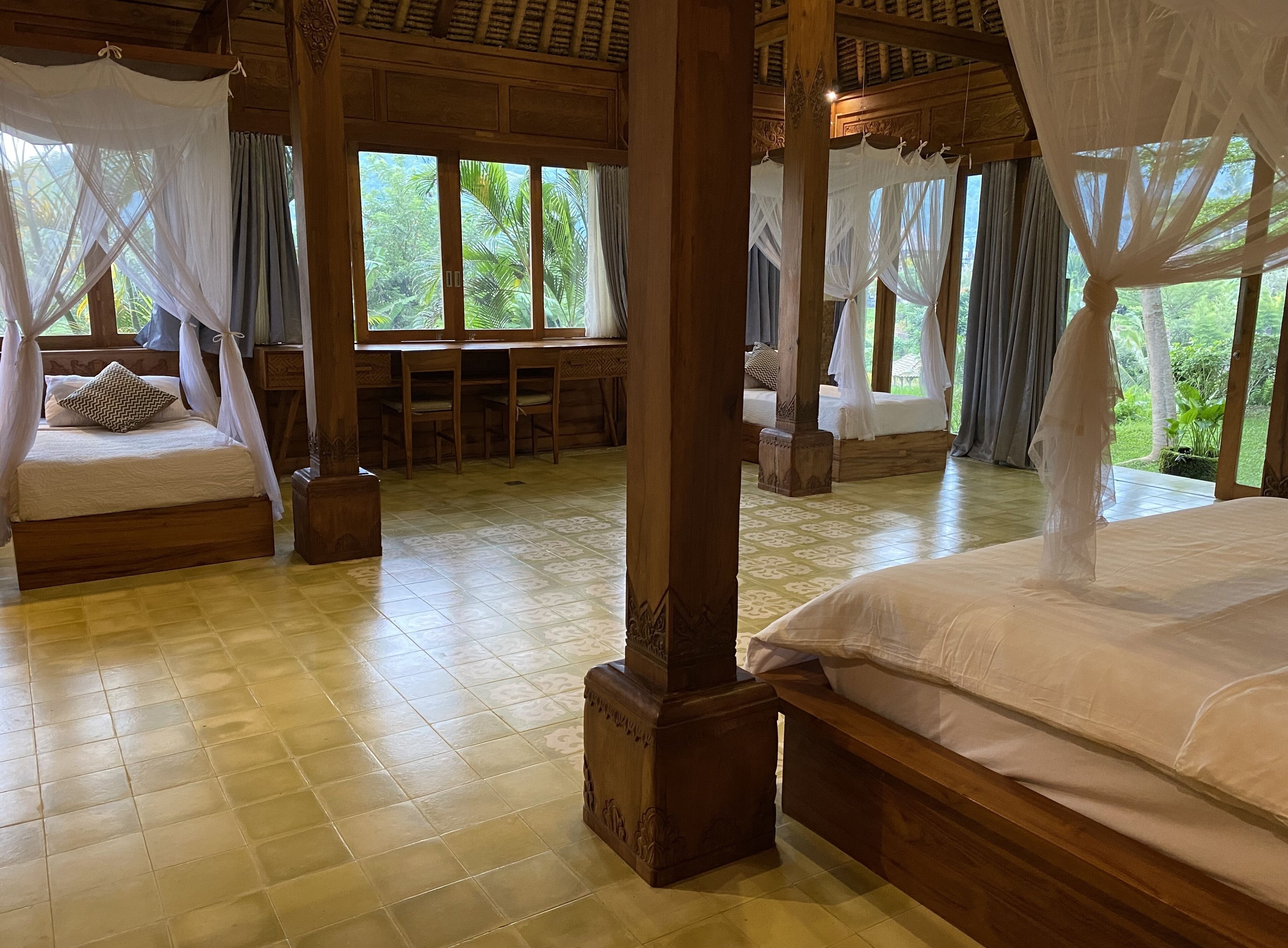 Une chambre dotée de deux lits, chacun surmonté d’un baldaquin, avec un plancher en bois et de grandes fenêtres donnant sur un paysage verdoyant.