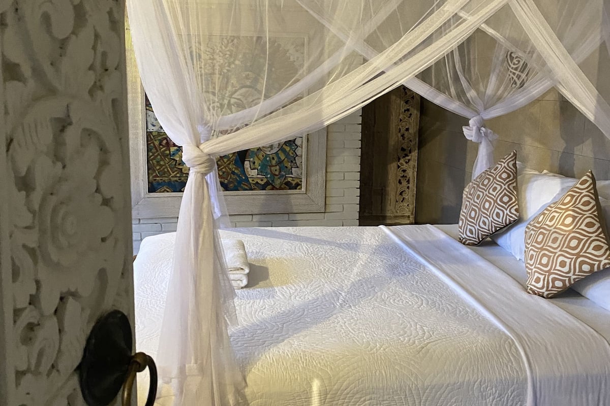 Una cama con dosel, cojines estampados y una pared decorativa.