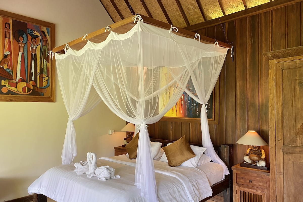 Una cama con dosel y cuatro columnas, con ropa de cama blanca y un arreglo decorativo de almohadas con forma de cisne.