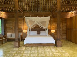 Una cama con dosel de madera, flanqueada por mesitas de noche con lámparas, en una habitación con paredes de madera y suelo de baldosas estampadas.