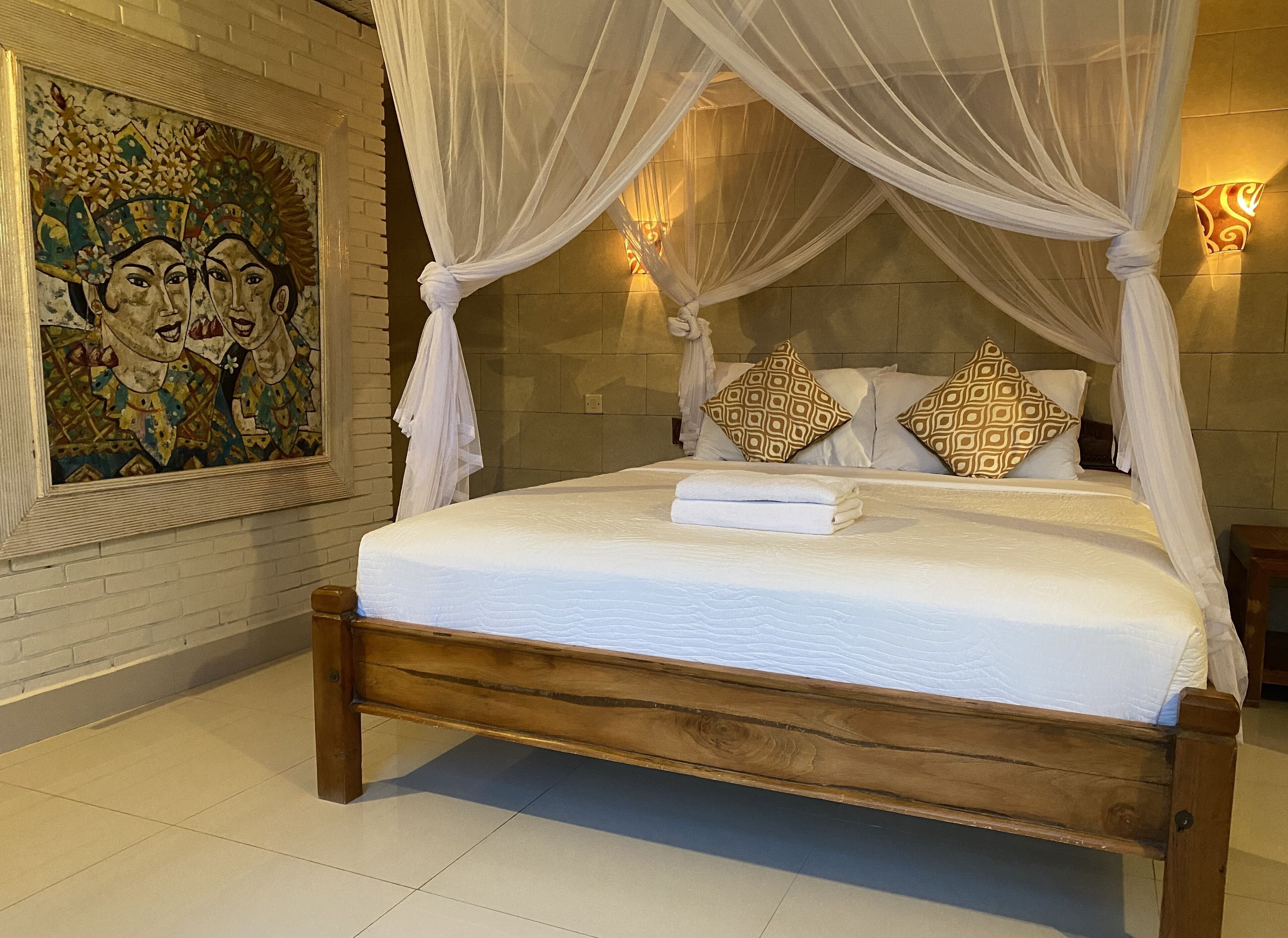 Een bed met houten frame en witte beddengoed, een wandlamp en een decoratief schilderij.