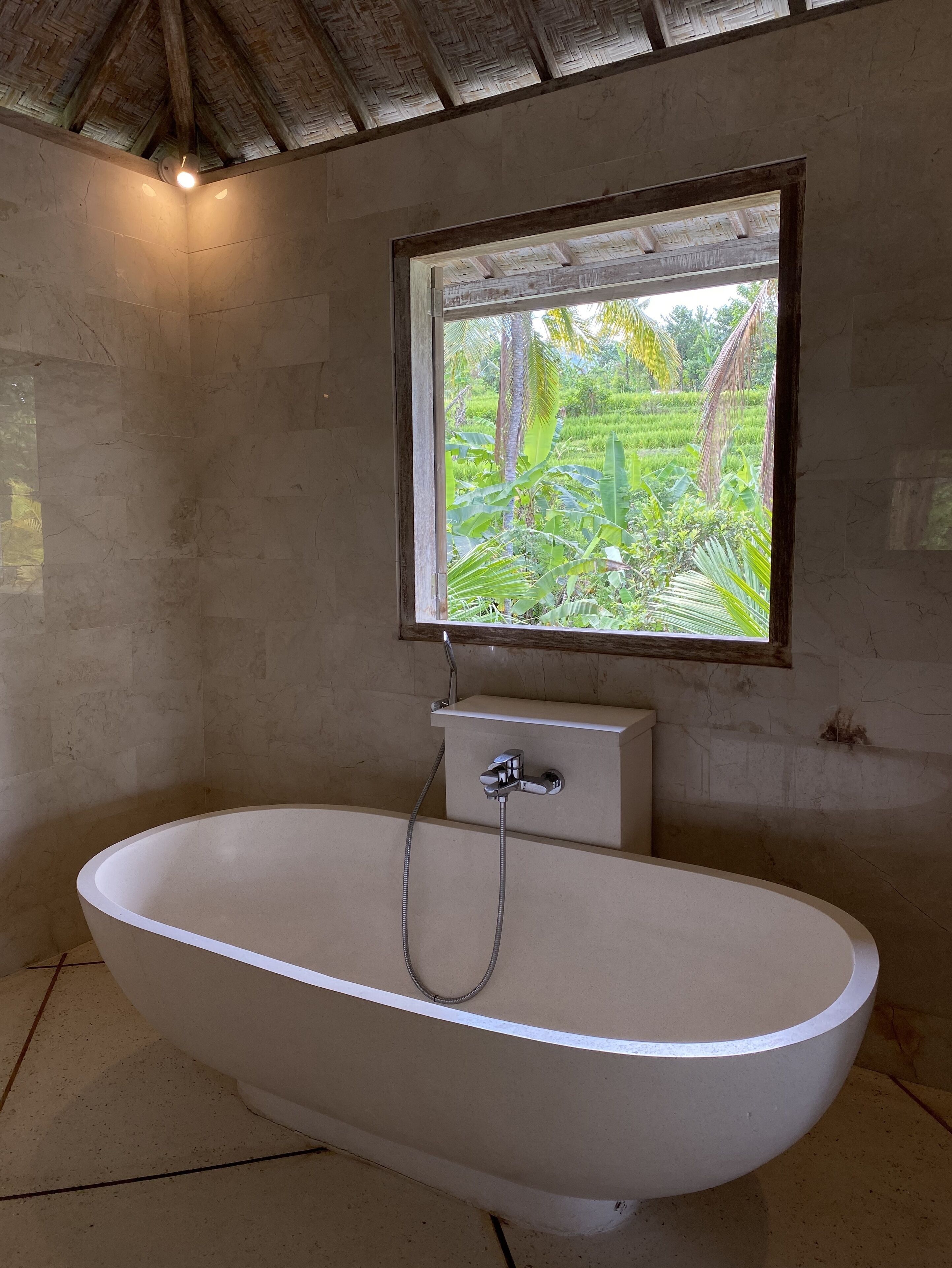Un baño con una bañera independiente, un ventanal con vistas a un jardín exuberante y un techo de madera.