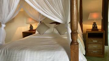 A four-poster canopy bed with white linens, two nightstands with lamps, and a wooden dresser with drawers.