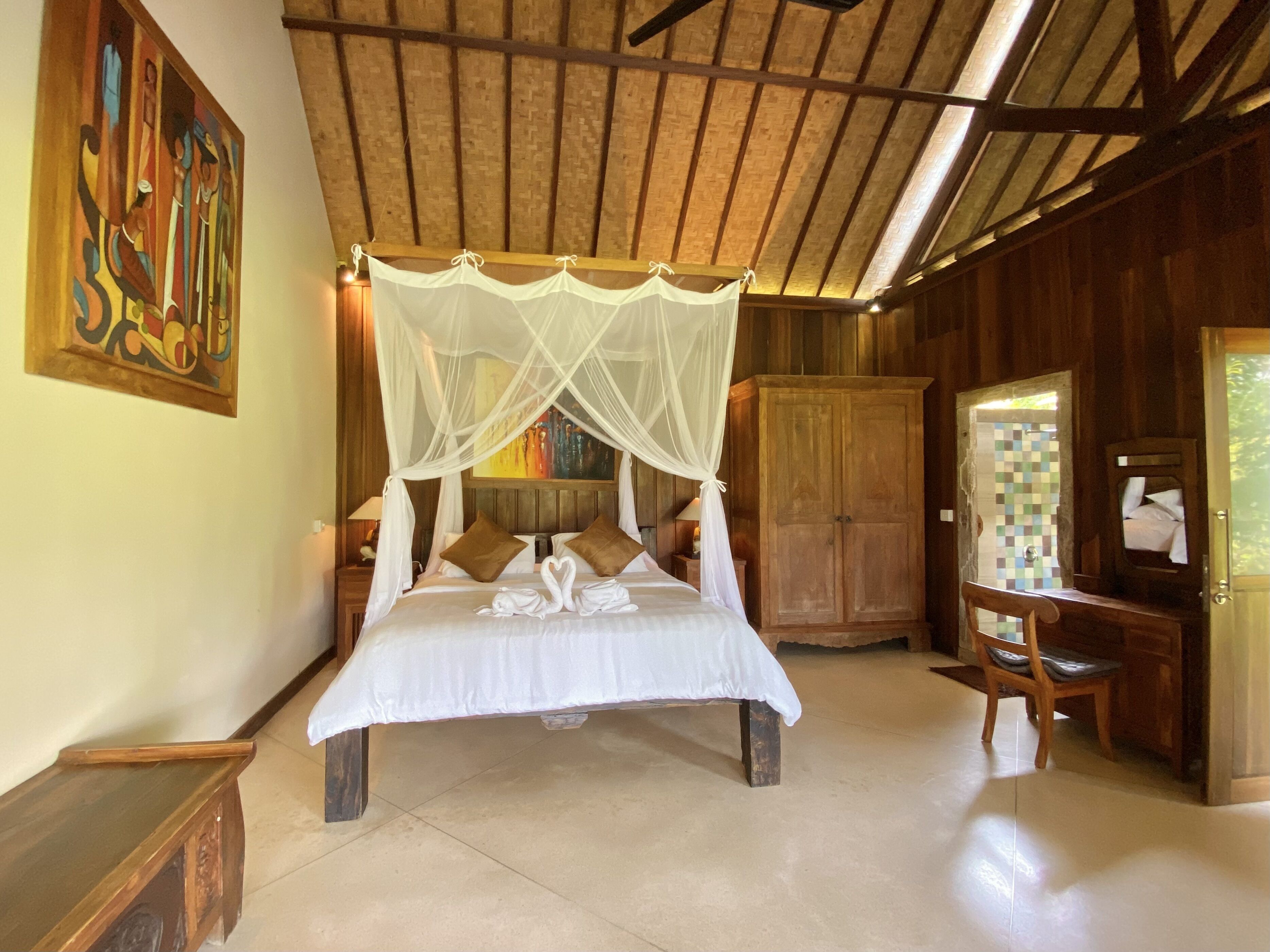 A spacious bedroom with a large bed, a wooden wardrobe, a vanity with a mirror, and a painting on the wall.