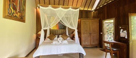 A spacious bedroom with a large bed, a wooden wardrobe, a vanity with a mirror, and a painting on the wall.