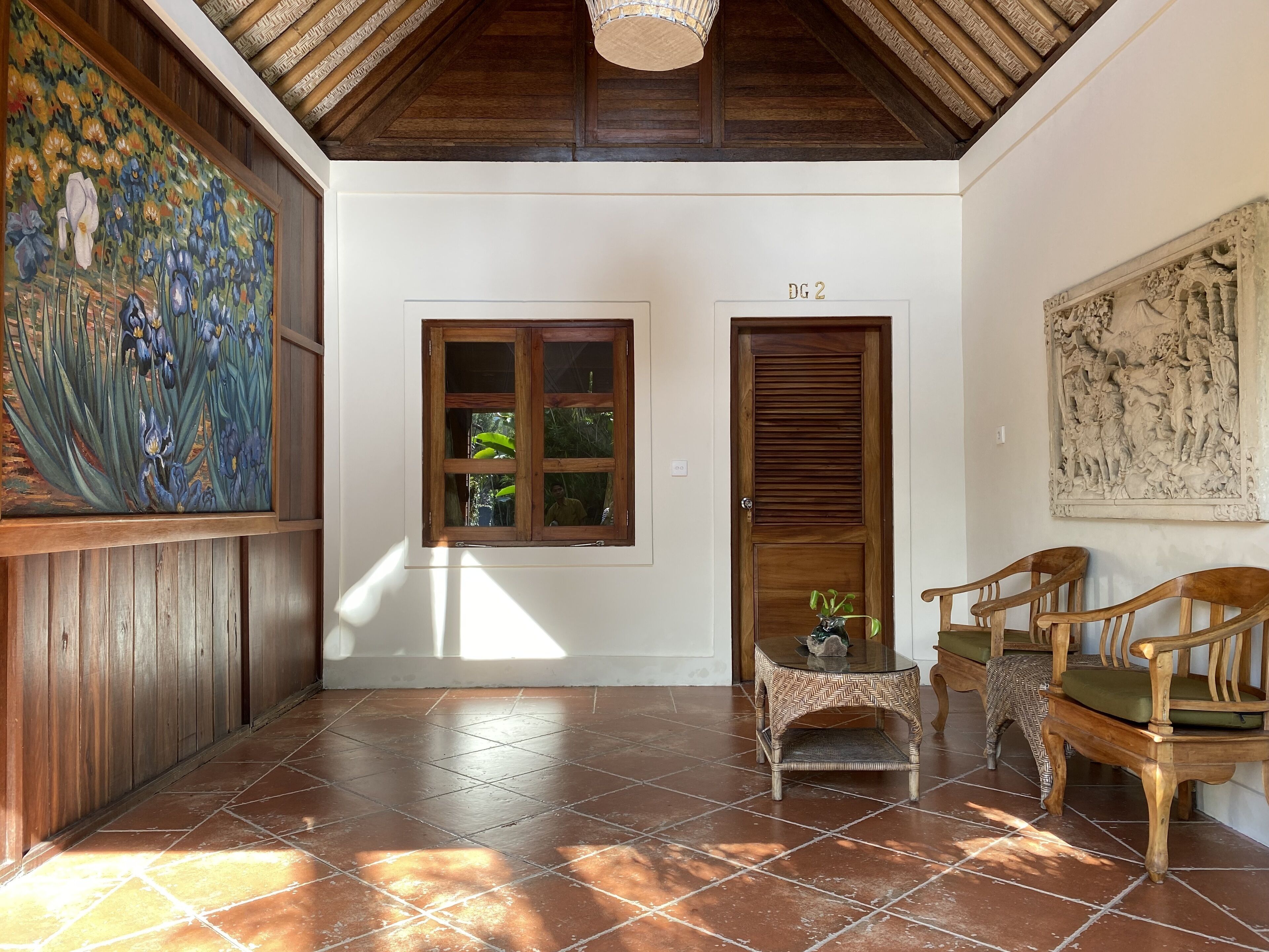 A hallway with a wooden door labeled "DG 2", a window with a view of greenery, and a painting of flowers on the left wall.