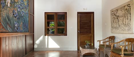 A hallway with a wooden door labeled "DG 2", a window with a view of greenery, and a painting of flowers on the left wall.
