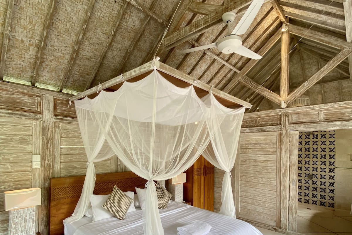 Habitación con cama bajo un dosel, paredes de madera y ventilador de techo.
