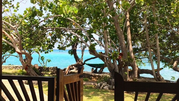 A wooden gate leading to a beach area with a hammock and a pair of shoes on the ground. - Little Bay Cabins (Little Bay)