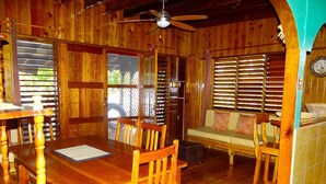 A wooden interior with a dining table, chairs, a sofa, and a ceiling fan. - Little Bay Cabins (Little Bay)