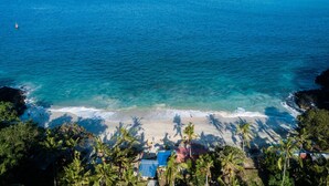 Ein Strand mit klarem, blauem Wasser, Palmen und einigen Gebäuden im Vordergrund.