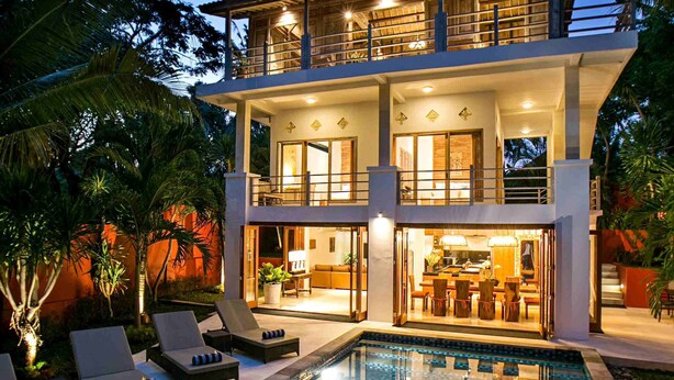 Ein zweistöckiges Haus mit Swimmingpool, Liegestühlen und Essbereich.