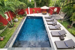 A rectangular swimming pool with clear blue water, surrounded by a red wall and lush greenery. - Casa Mimba (Padangbai)