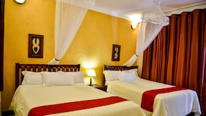 A hotel room with two beds, a nightstand with a lamp, and a mosquito net over the window. - Cari Hotel (Kigali)