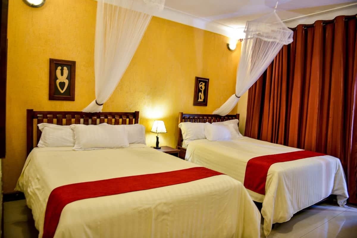 A hotel room with two beds, a nightstand with a lamp, and a mosquito net over the window.