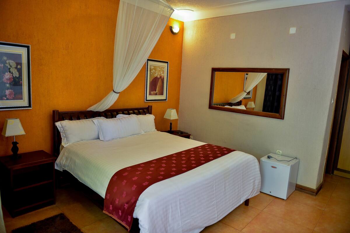 A hotel room with a bed, nightstands, a bedside lamp, a heater, a mirror, and a picture on the wall.