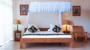 A bed with a canopy, two bedside lamps, a chair, and two framed pictures on the wall.