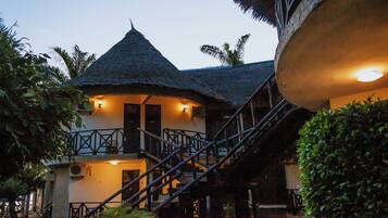 A building with a thatched roof, a staircase leading to a balcony, and a well-lit entrance.