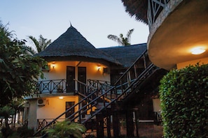 A building with a thatched roof, a staircase leading to a balcony, and a well-lit entrance. - Millennium Sea Breeze Resort (Bagamoyo)