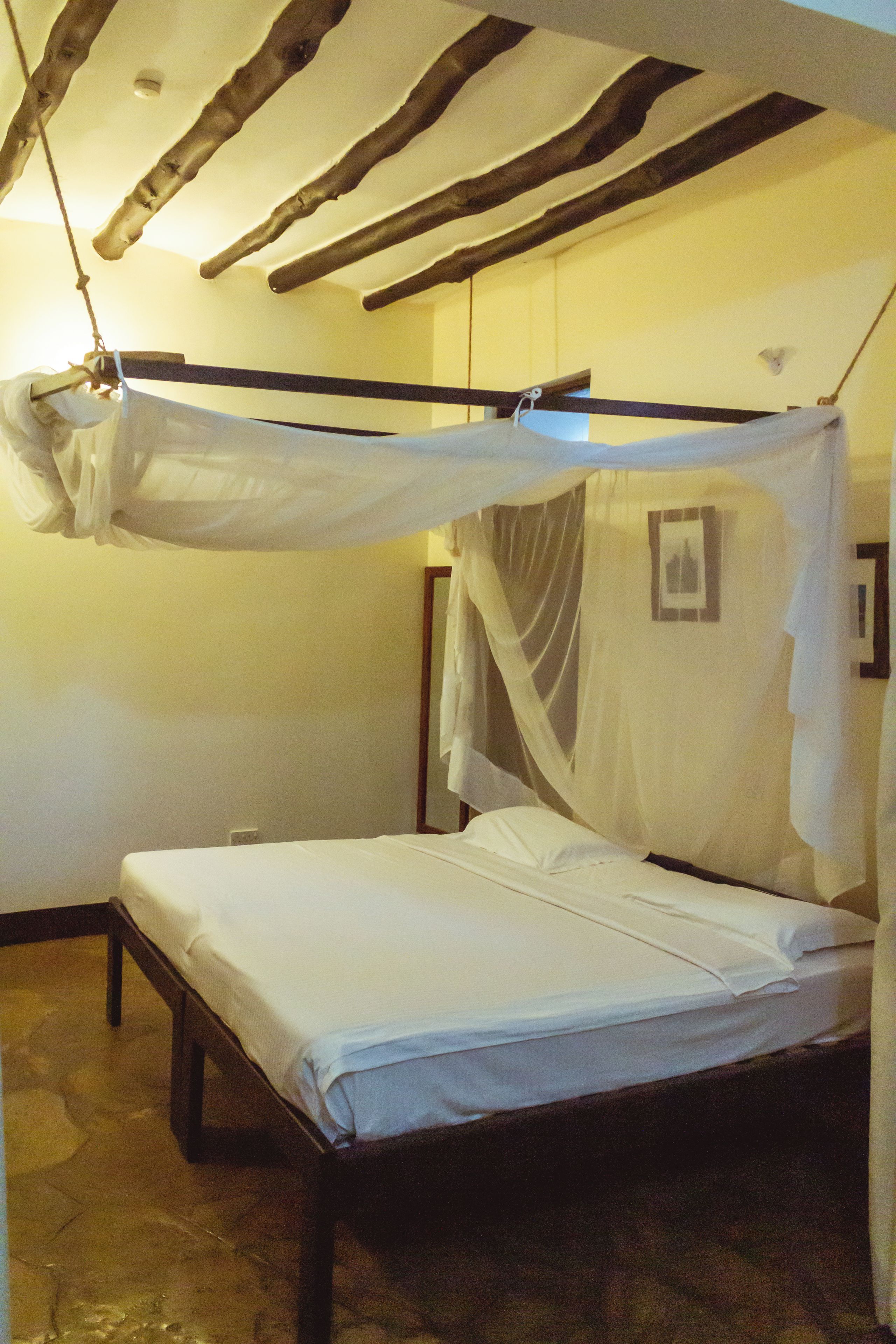 A room with a bed under a canopy, a wooden ceiling, and a wall-mounted picture.