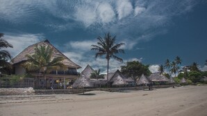 Un complexe hôtelier en bord de mer, avec des bungalows aux toits de chaume, des palmiers et une plage de sable.