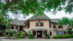 A resort with a thatched roof, a sign reading 'Millennium Sea Breeze Resort,' and a staircase leading to the entrance.