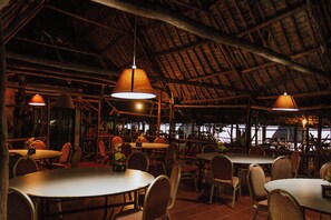 Un espace de restauration intérieur avec des tables et des chaises rondes, des poutres en bois au plafond et des lampes suspendues.