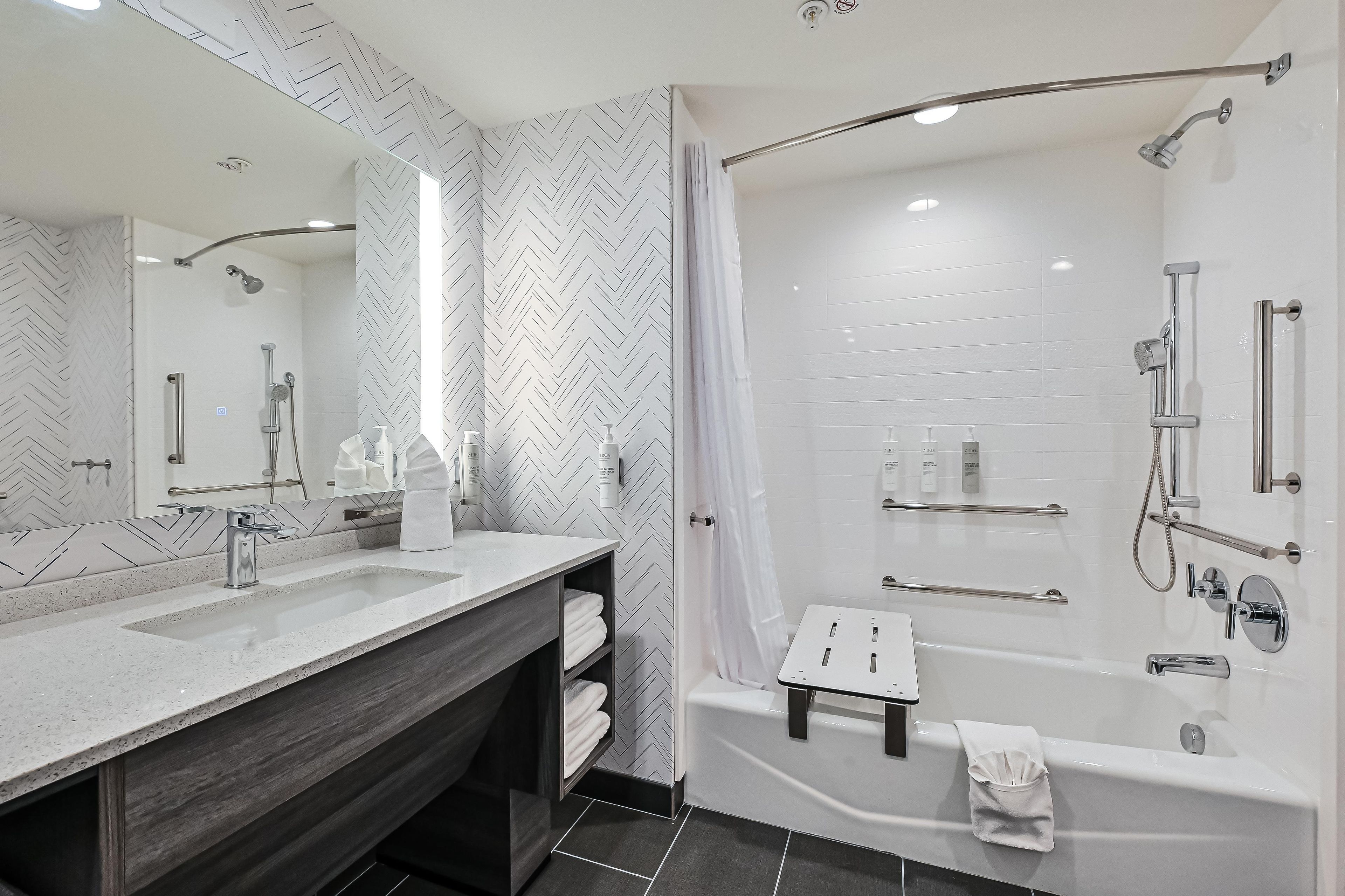 A modern bathroom with a large mirror, dual sinks, a shower area, and a towel rack.