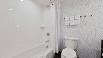 A modern bathroom with a bathtub, toilet, and shower.