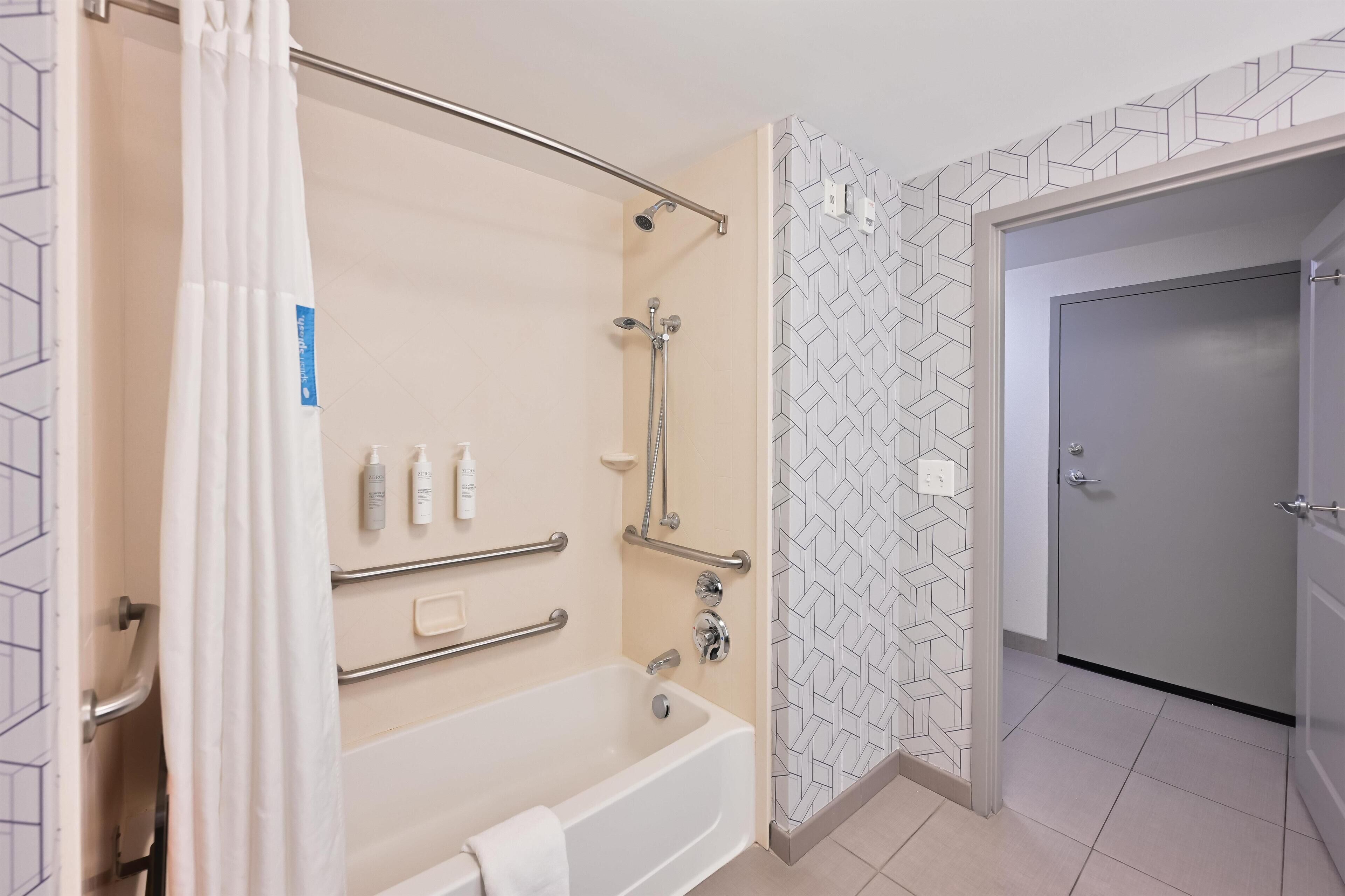 A modern bathroom with a bathtub, shower, and handrails.