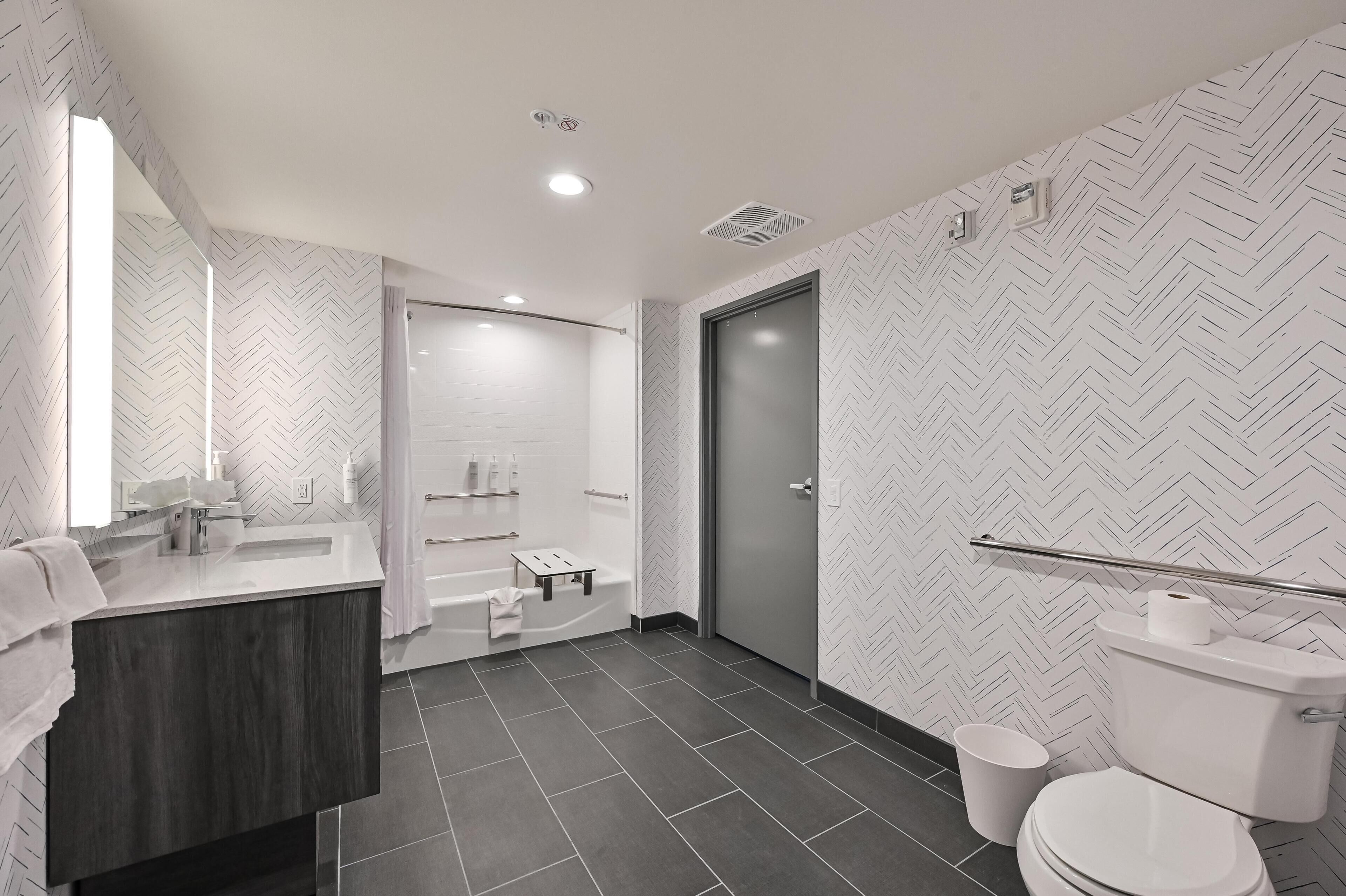 Un baño moderno con tocador de madera oscura, zona de ducha y retrete.