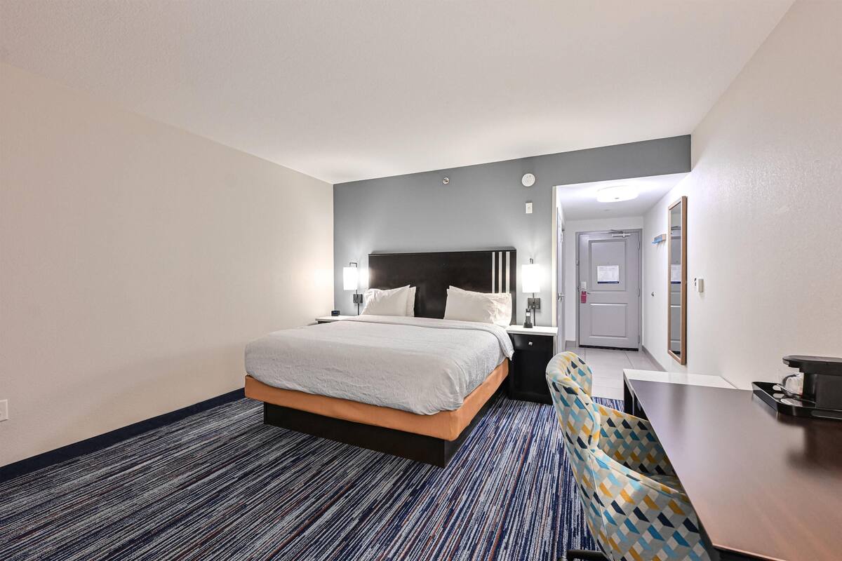 Quarto de hotel com cama, mesas de cabeceira, escrivaninha e cadeira.