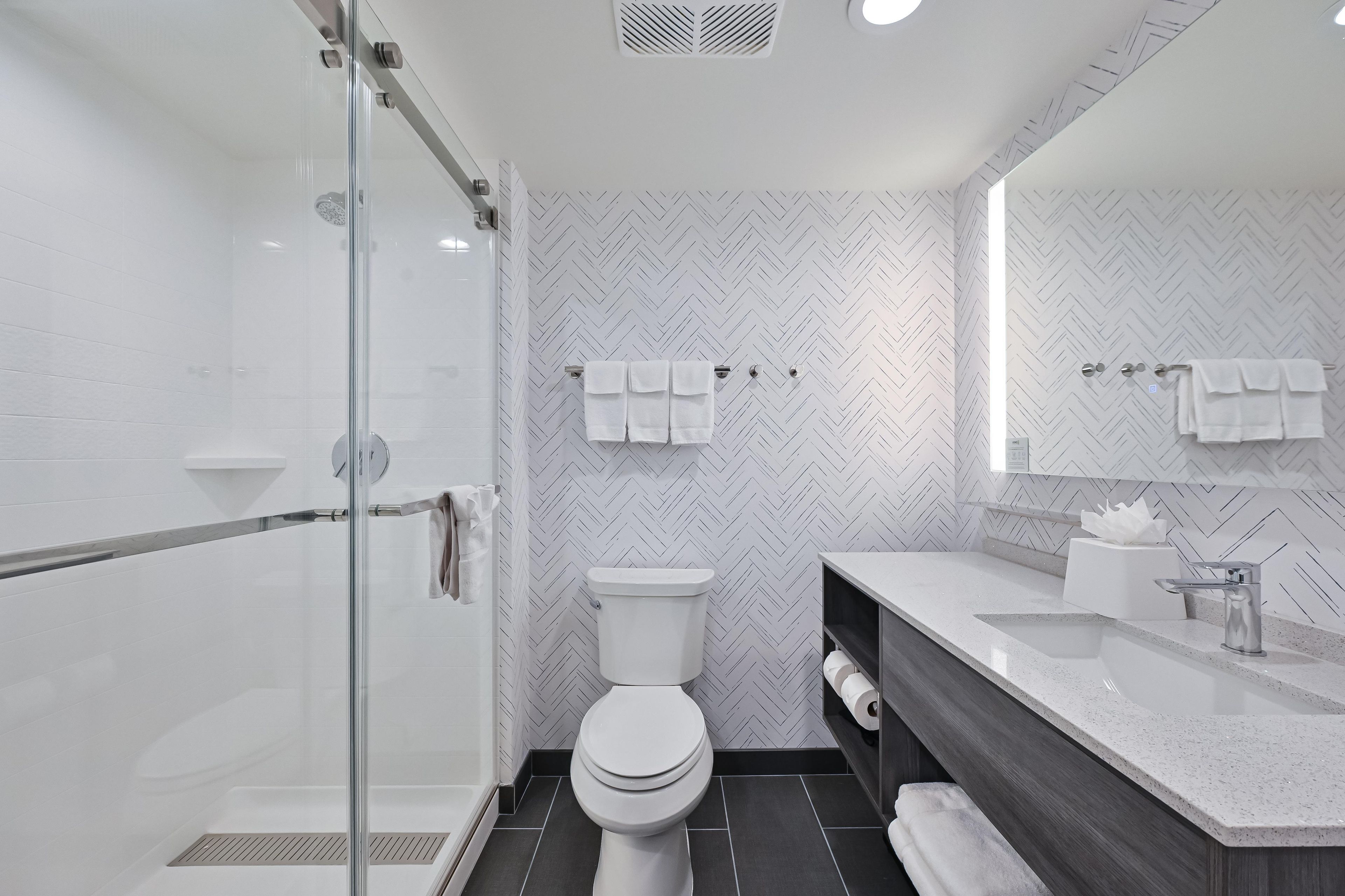 Un baño moderno con cabina de ducha de vidrio, inodoro blanco, tocador con espejo y perchero para toallas.