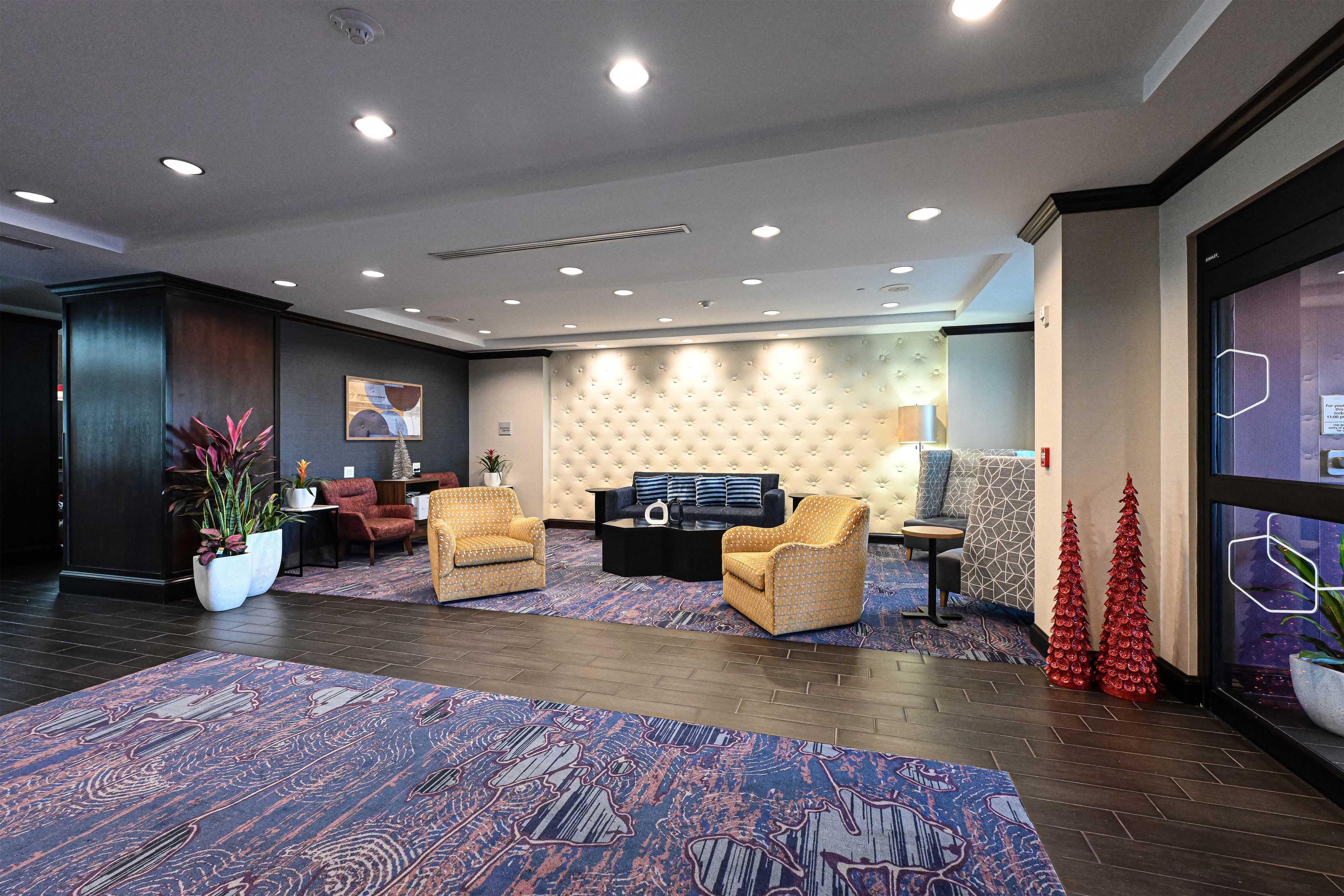 A modern hotel lobby with a seating area, a large rug, and a Christmas tree.