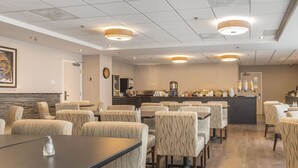 A restaurant with multiple tables and chairs, a counter with a coffee machine, and a clock on the wall. - Quality Inn Sept-Îles (Uashat)