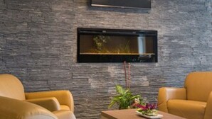 A modern living room with a stone wall, a flat-screen TV mounted above a fireplace, and two leather armchairs. - Quality Inn Sept-Îles (Uashat)