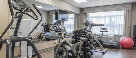 A gym with cardio machines, weights, and a large mirror.