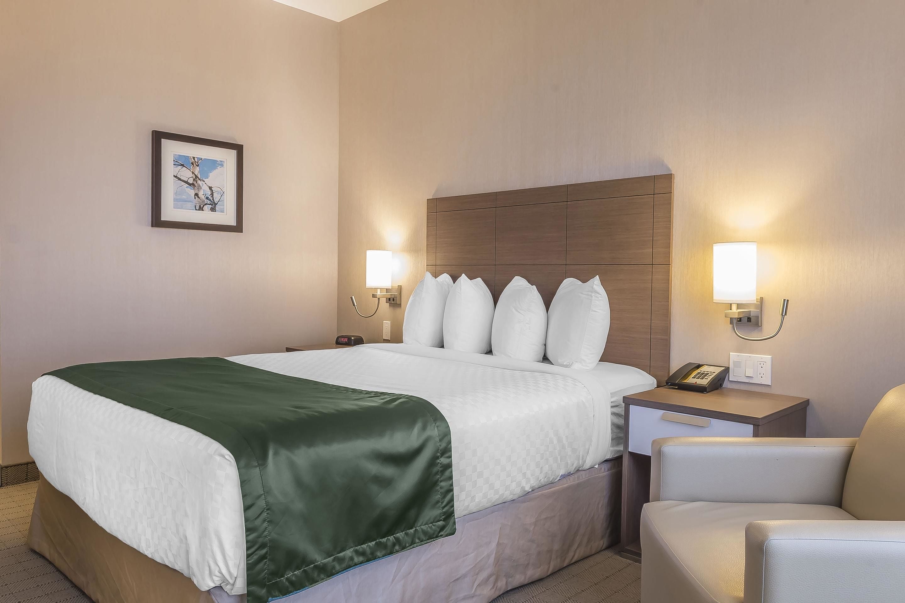 A hotel room with a large bed, a nightstand with a lamp, a chair, and a framed picture on the wall.