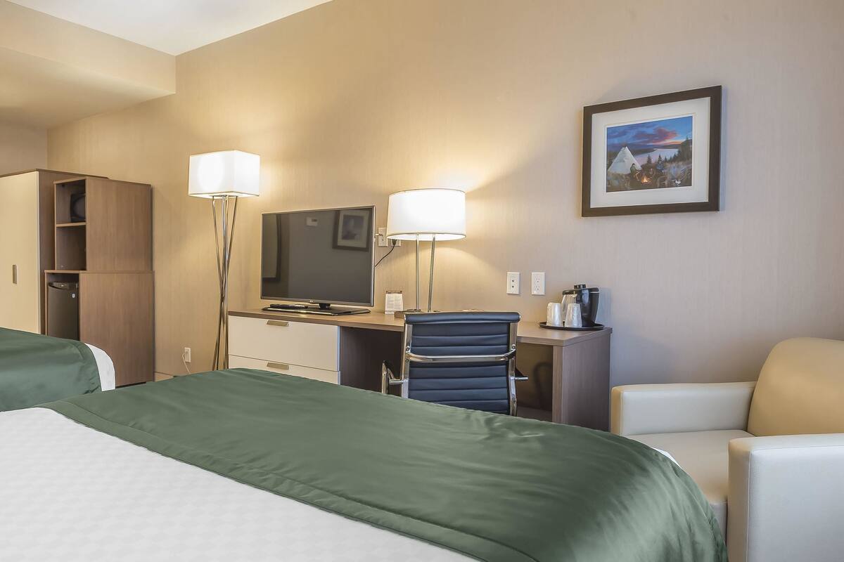 Habitación de hotel con dos camas, un escritorio con computadora, una silla, una lámpara y un cuadro en la pared.