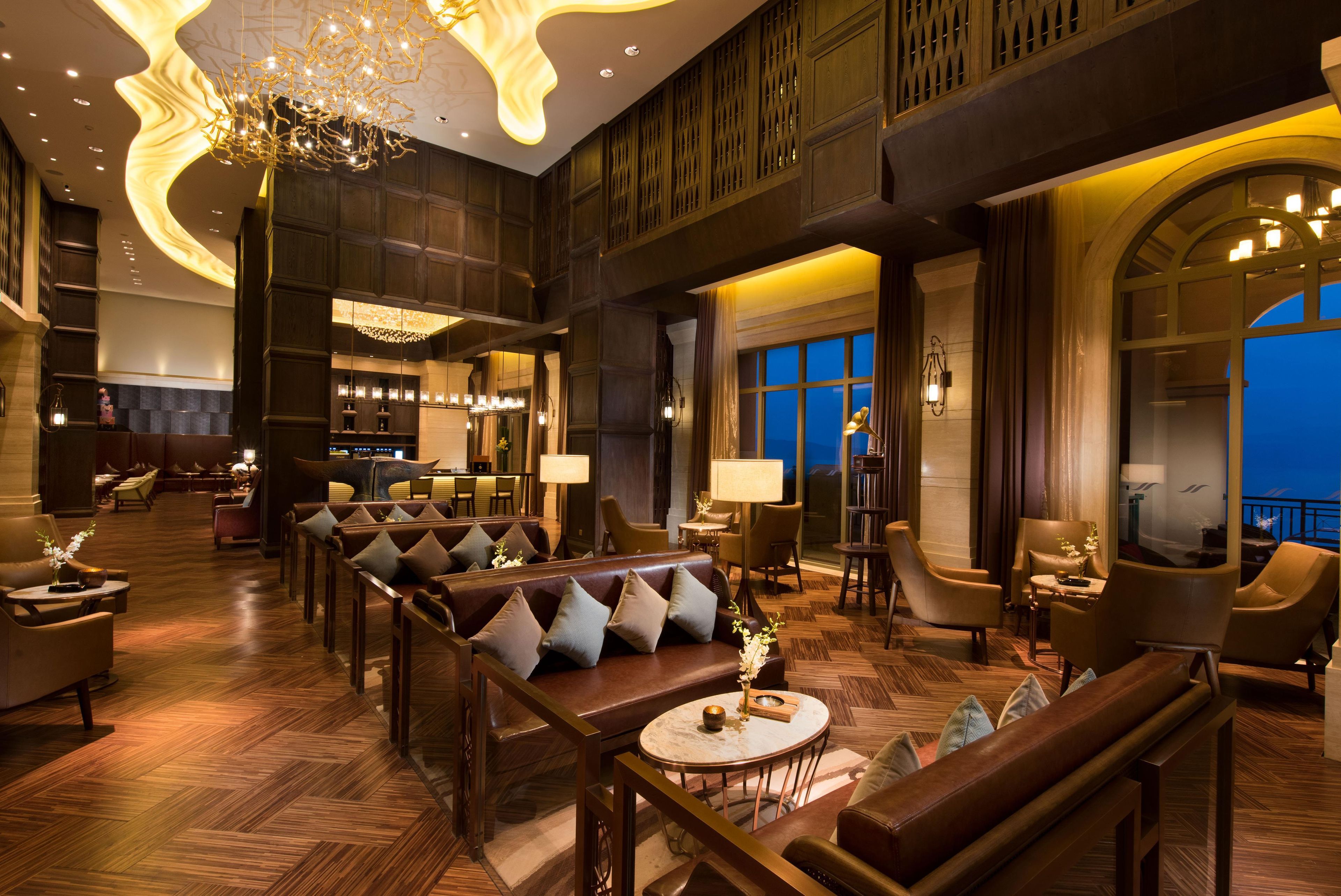 Een ruime lobby met een hoge plafond, moderne verlichtingsarmaturen en een zithoek met leren banken en fauteuils.