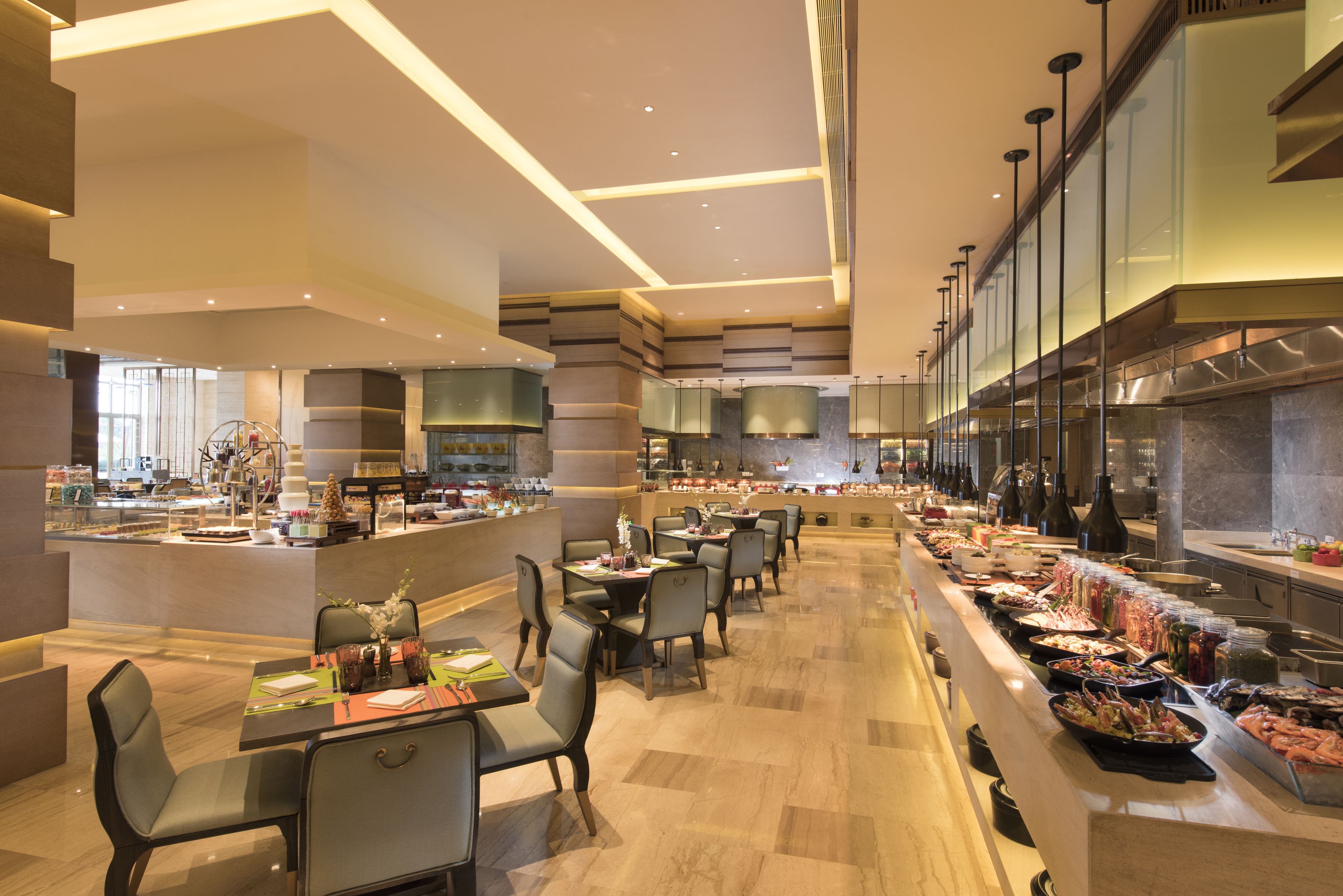 A modern restaurant with a long counter, multiple tables, and a variety of food items displayed.