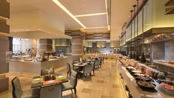 A modern restaurant with a long counter, multiple tables, and a variety of food items displayed.