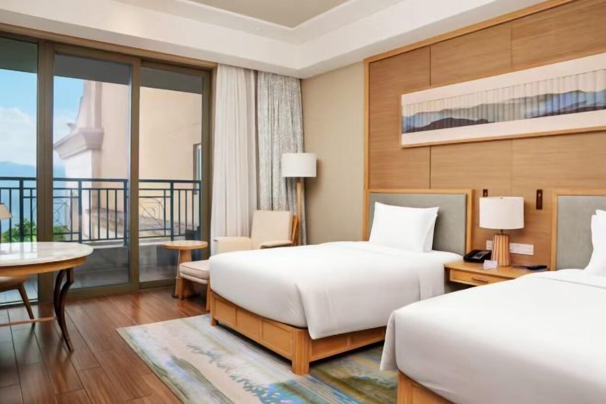 Habitación de hotel con dos camas, un balcón, una mesa redonda y vistas al mar.
